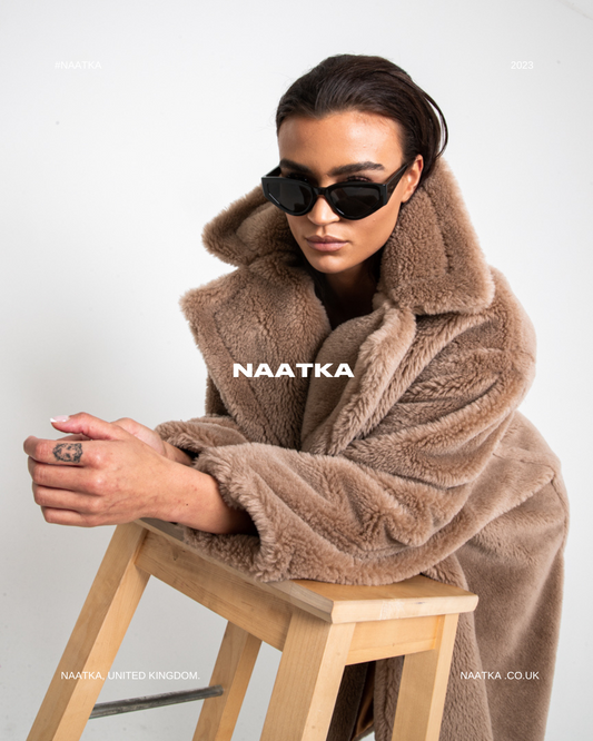 model leaning over wooden stool in a fluffy brown teddy coat.
