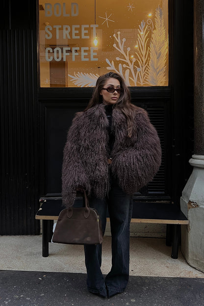 Person wearing a Mongolian sheep fur coat standing in front of a coffee shop entrance.
