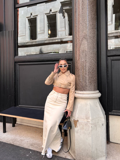 girl stood in front of black door with window wearing a cropped belted cream leather jacket and maxi skirt.