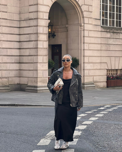 woman stood in street wearing a faded effect oversized ash-grey leather jacket holding a bag.