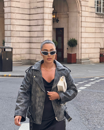 woman walking in street wearing a faded effect oversized ash-grey leather jacket holding a bag.