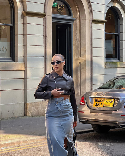 girl stood in street next to a taxi wearing a cropped belted leather jacket and midi denim skirt with rips.