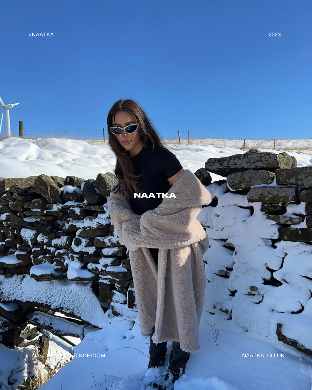 a woman wearing a beige teddy coat standing on top of a snow covered ground.