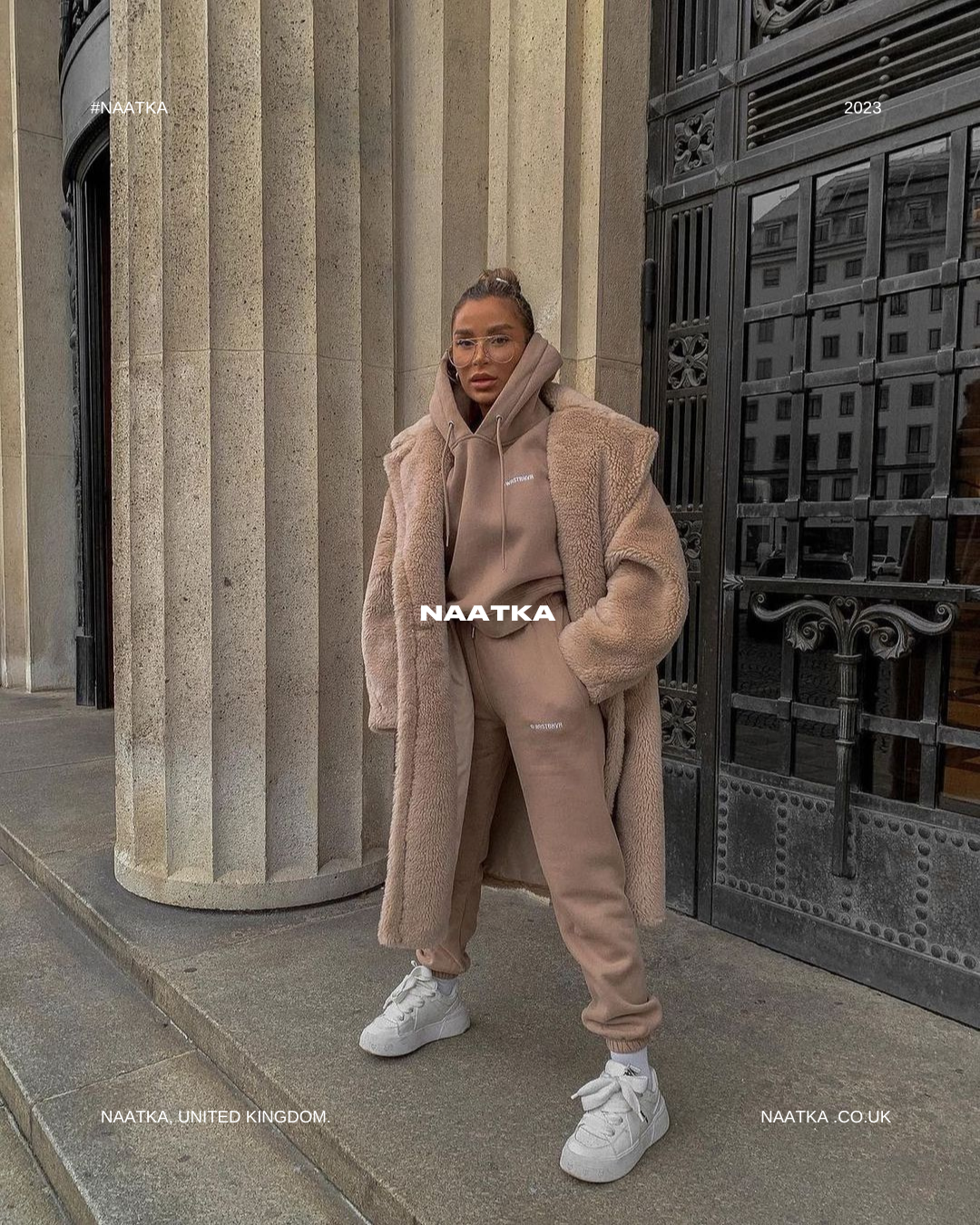 a woman standing on a sidewalk wearing a big teddy coat and tracksuit.