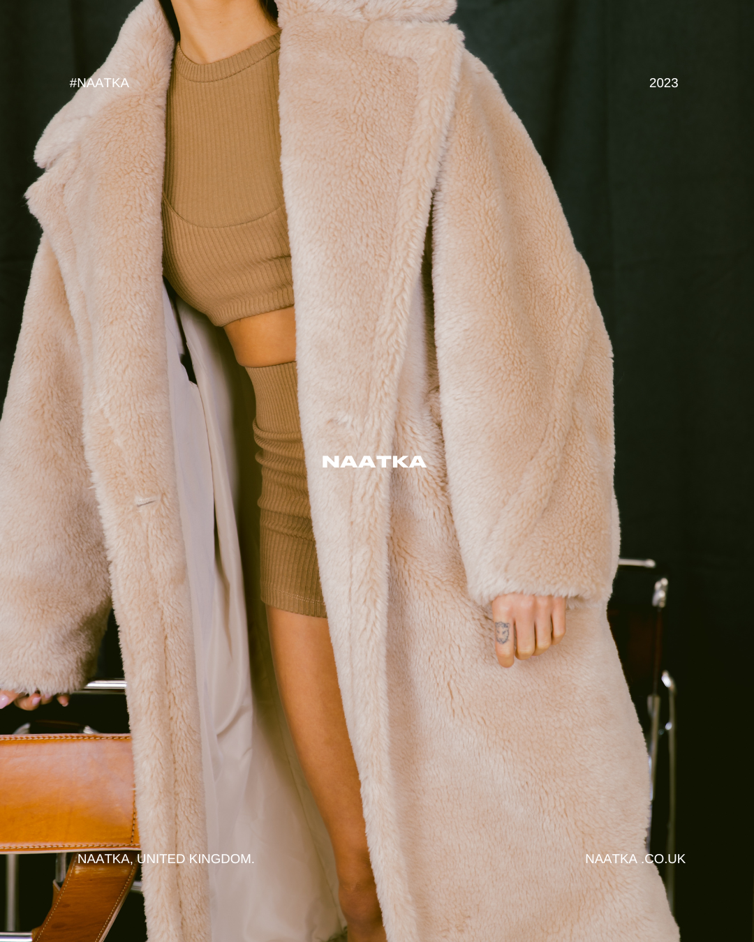 detail shot of a model standing in front of a black curtain wearing a long beige teddy coat.